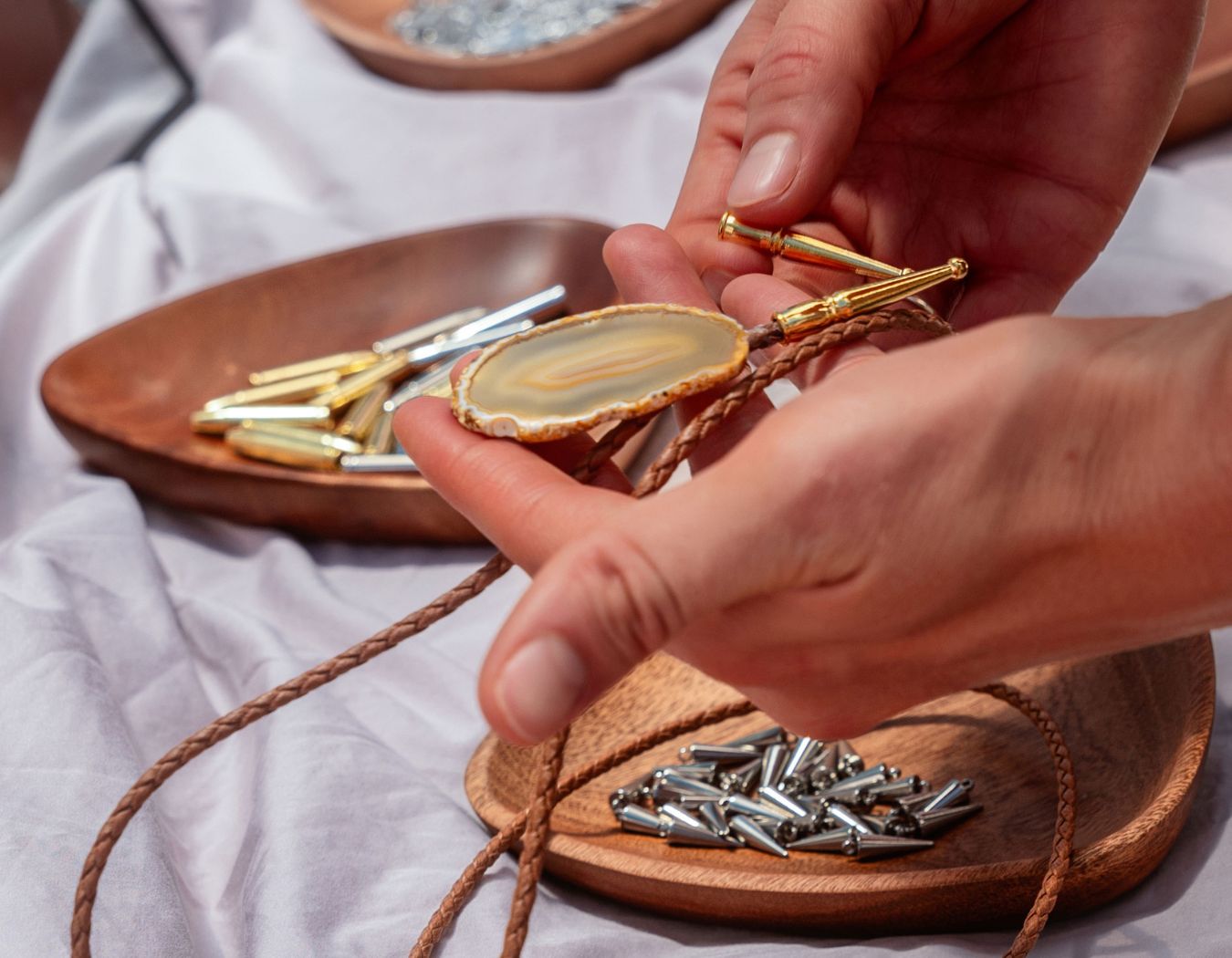 Hands assembling a custom bolo tie with agate slide, braided leather cord, and gold tips