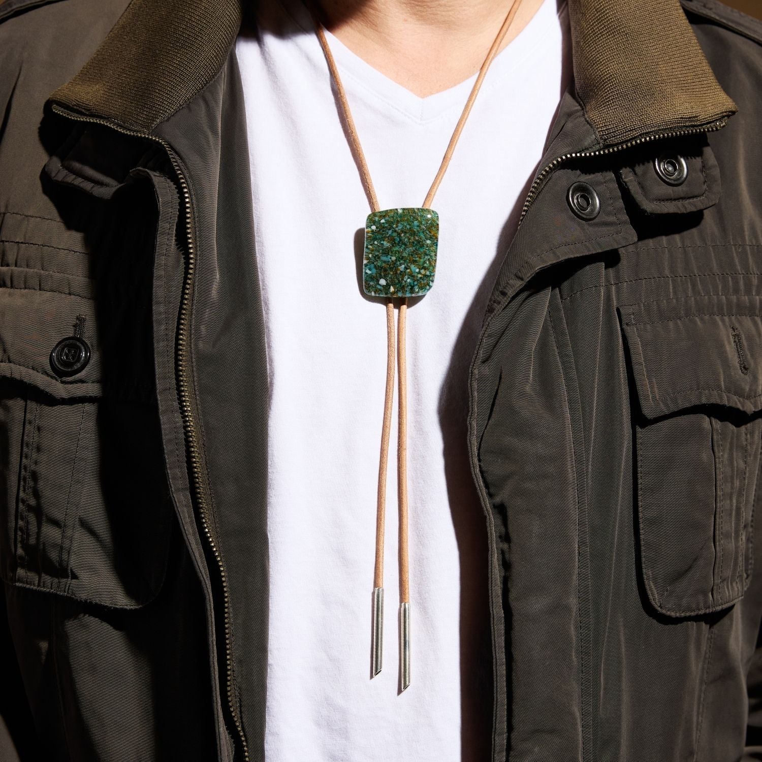 Man wearing turquoise stone bolo tie with olive utility jacket casual styling